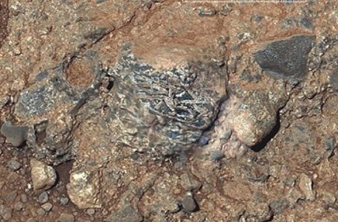 Clast ígnea llamada Harrison incrustado en una roca en el cráter Gale, Marte, Muestra cristales alargados de feldespato de tonos claros. Clast ígnea llamada Harrison incrustado en una roca en el cráter Gale, Marte, Muestra cristales alargados de feldespato de tonos claros.