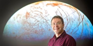 El Dr Jonti Horner delante de una imagen del satélite de Júpiter, Europa. "Es otro lugar en nuestro sistema solar, donde podría haber vida", dijo.